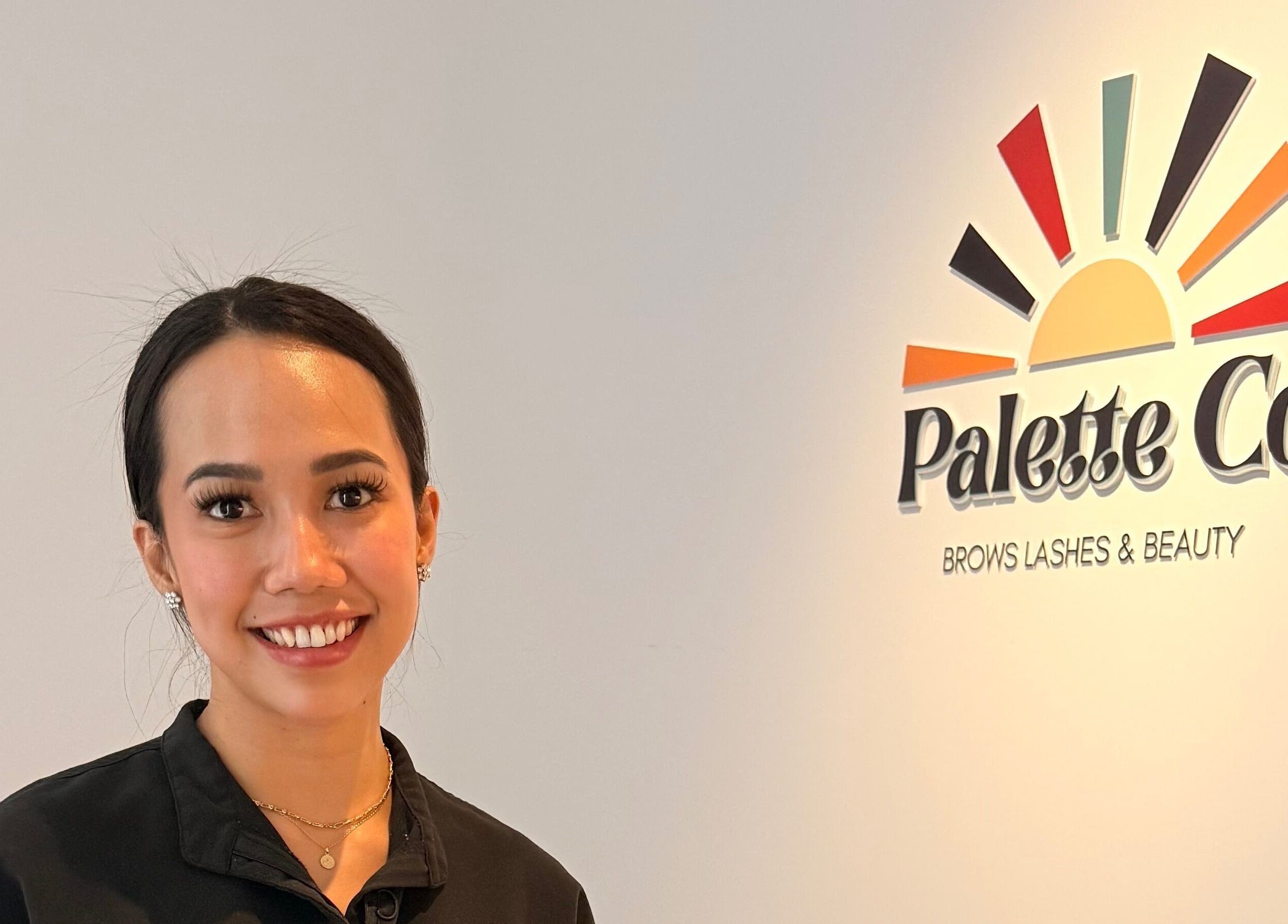 Smiling staff member at Palette Co, West End, Queensland, AU, next to colorful logo wall.