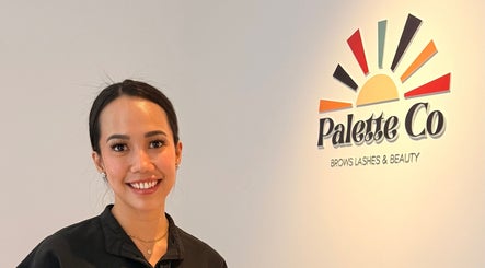 Smiling staff member at Palette Co, West End, Queensland, AU, next to colorful logo wall.