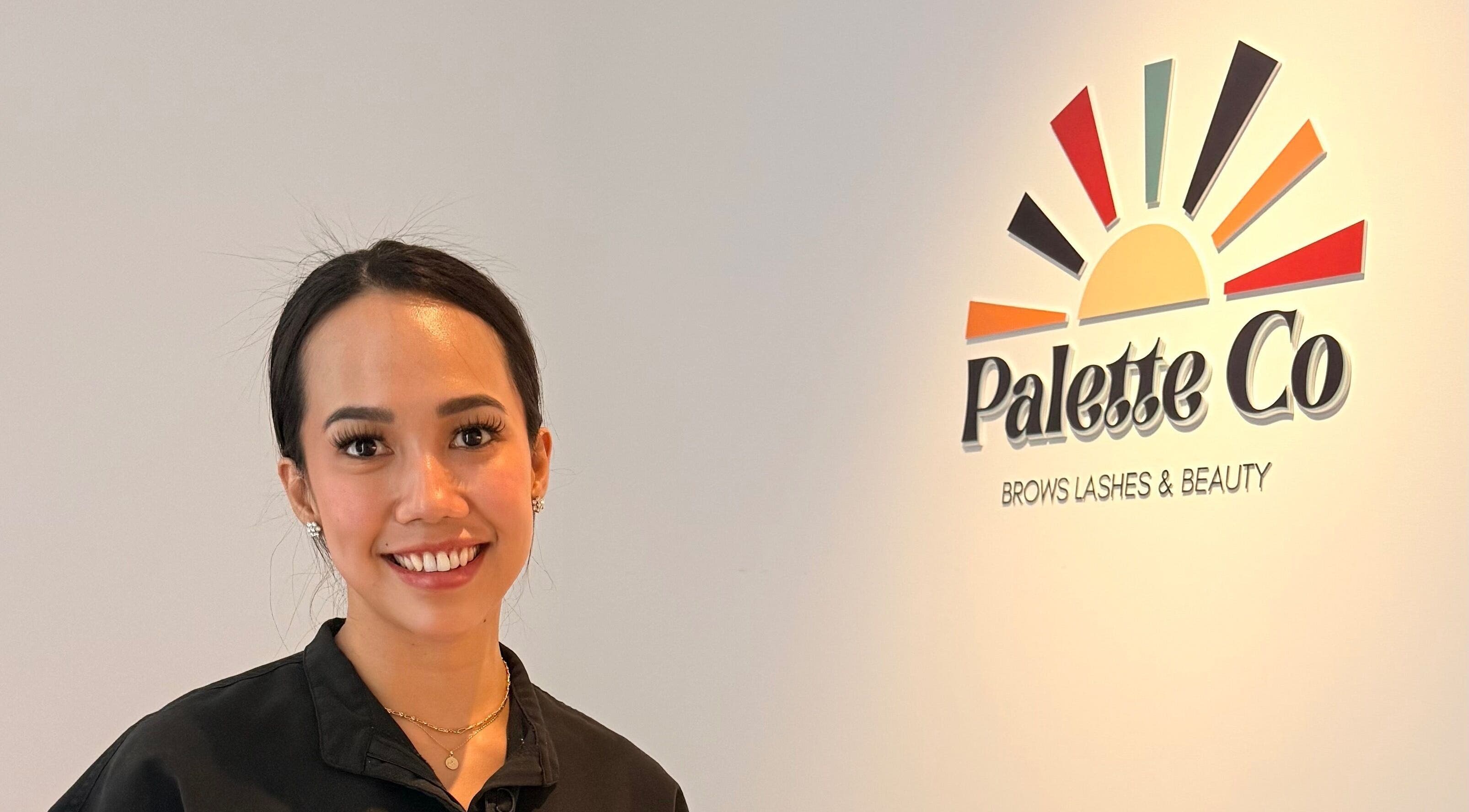 Smiling staff member at Palette Co, West End, Queensland, AU, next to colorful logo wall.