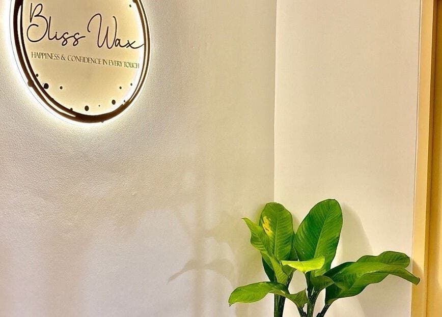 Bliss Wax logo warmly lit beside a green plant in ตำบล ศรีสุนทร, ภูเก็ต, TH spa entrance.
