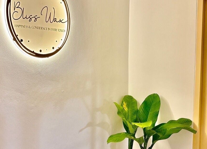 Bliss Wax logo warmly lit beside a green plant in ตำบล ศรีสุนทร, ภูเก็ต, TH spa entrance.