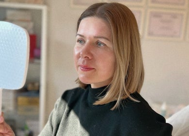 Woman examining skin with mirror at Kati Aesthetics in London, England, GB.