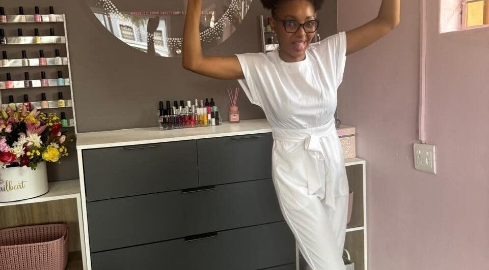 Smiling individual at Nailbeat & Co, Pretoria, Gauteng, ZA surrounded by nail polish and flowers.