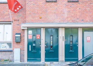 Entrance of Sy Relax Massage & Wellness in Amsterdam, Noord-Holland, NL, with red brick facade and green doors.