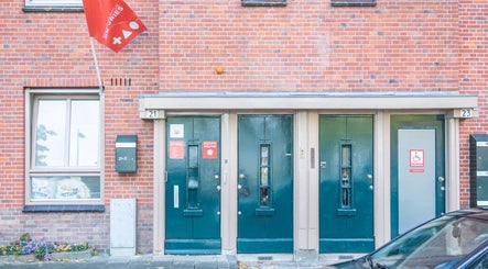 Entrance of Sy Relax Massage & Wellness in Amsterdam, Noord-Holland, NL, with red brick facade and green doors.