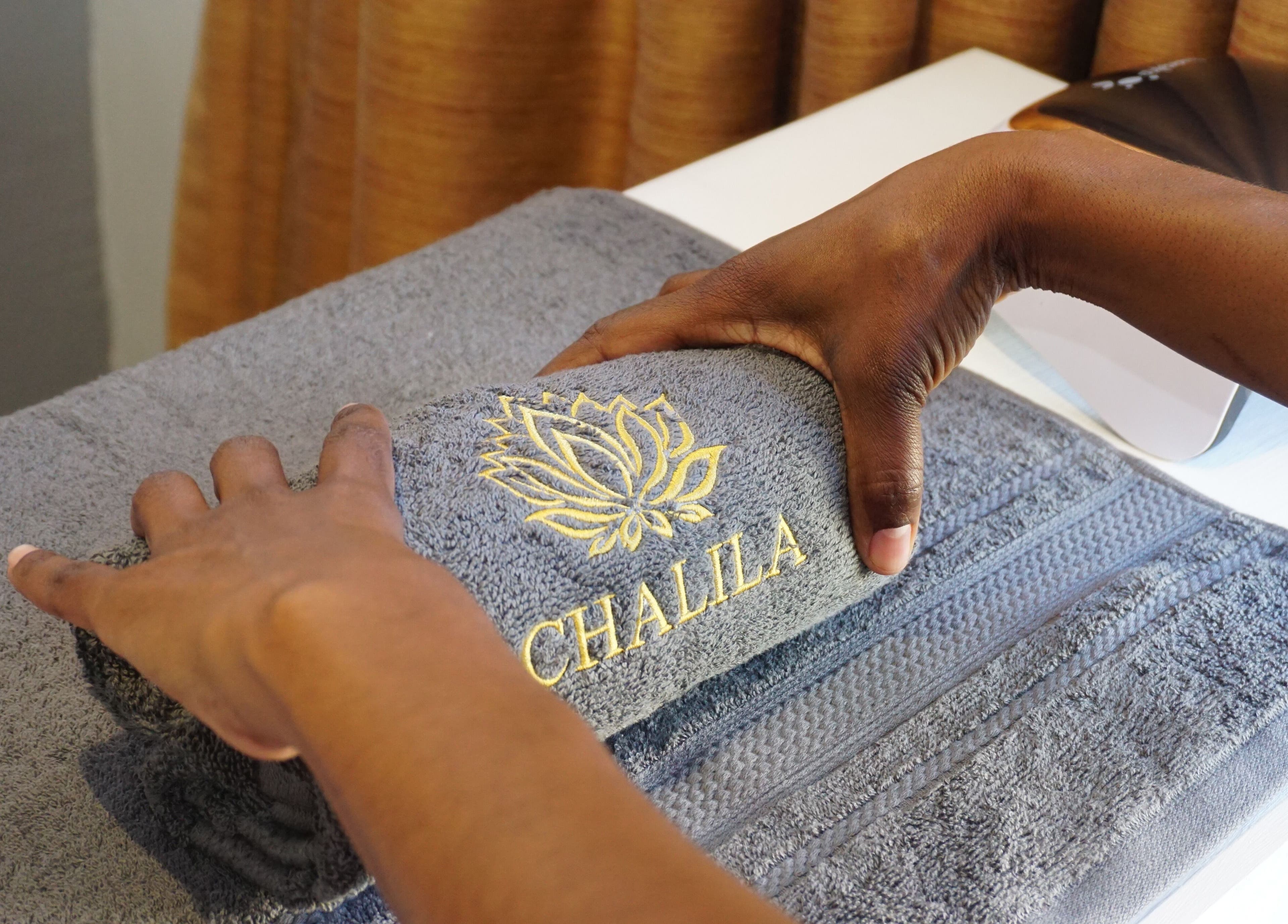 Towel with Chalila Wellness logo being rolled by hand at Cape Town, Western Cape, ZA spa.