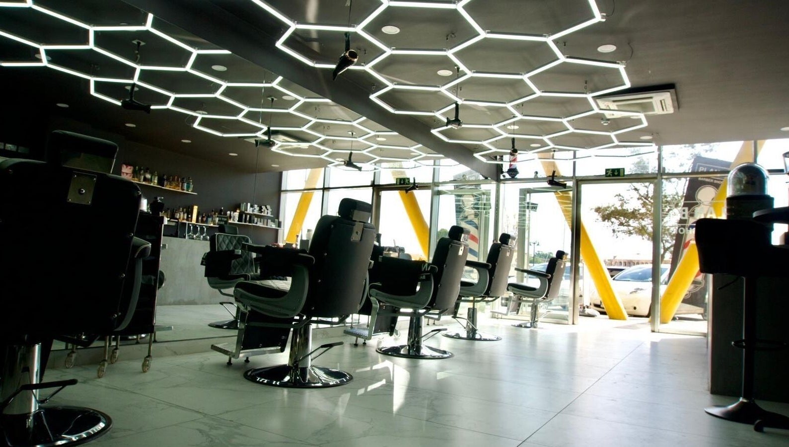 Modern barber chairs at PLAN B | THE STRAND, Tas-sliema, MT. Stylish interior with hexagonal ceiling lights.