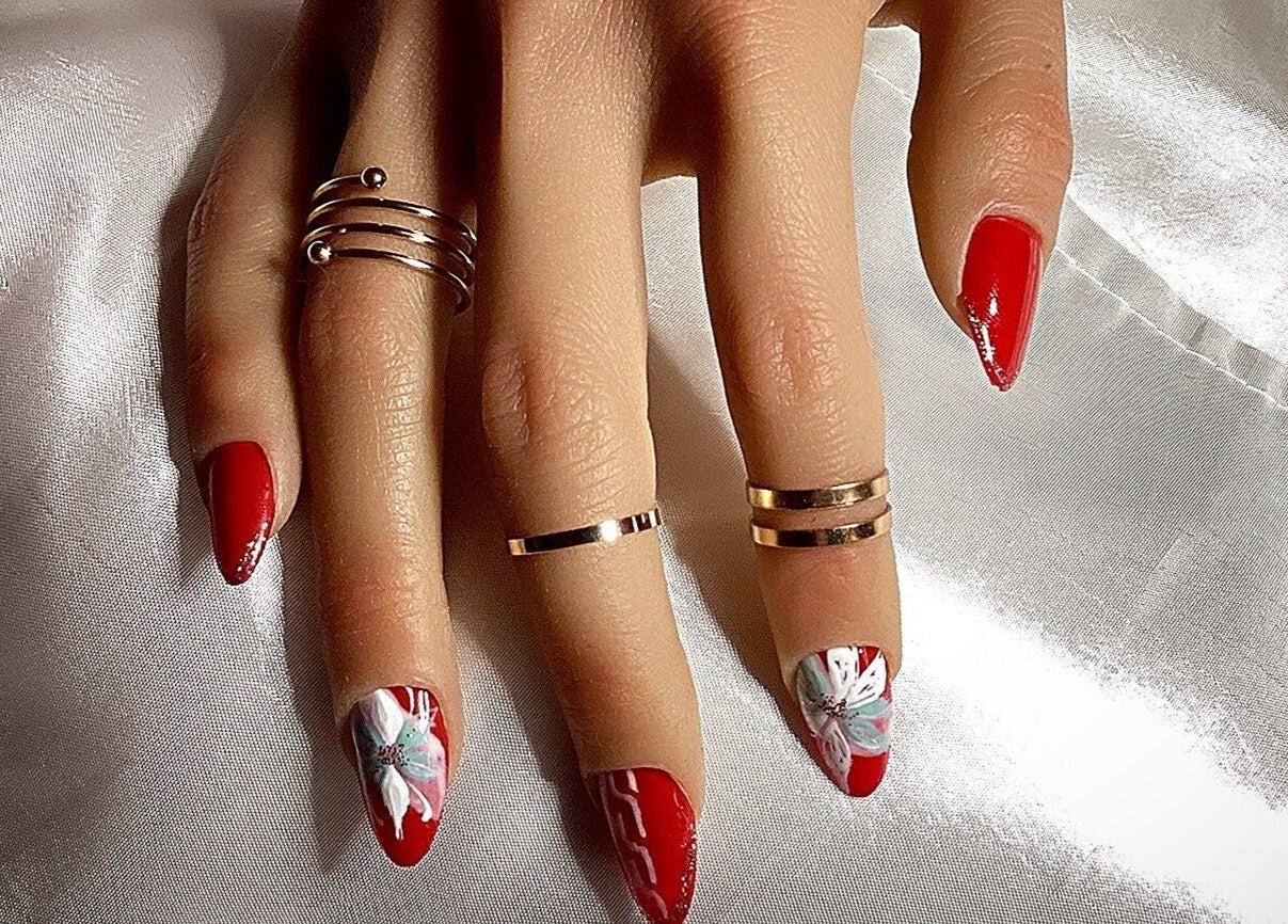 Nail art élégant à Od'île Beauté Bien-être, Cahors, Occitanie, FR, avec des motifs floraux sur fond rouge.