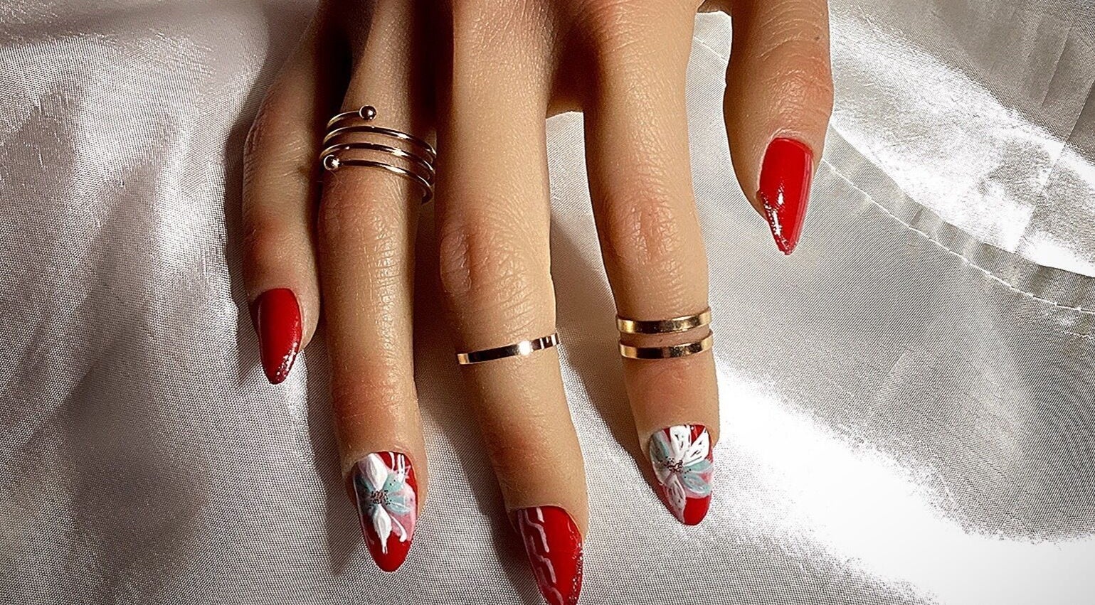 Nail art élégant à Od'île Beauté Bien-être, Cahors, Occitanie, FR, avec des motifs floraux sur fond rouge.