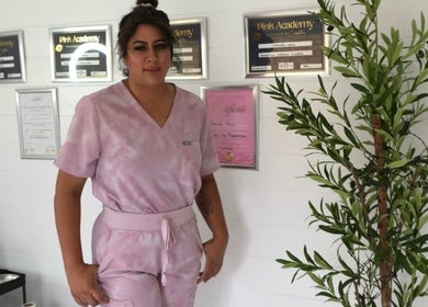 Professional at Shine By S, Peterborough, England, GB standing beside framed certifications and greenery.