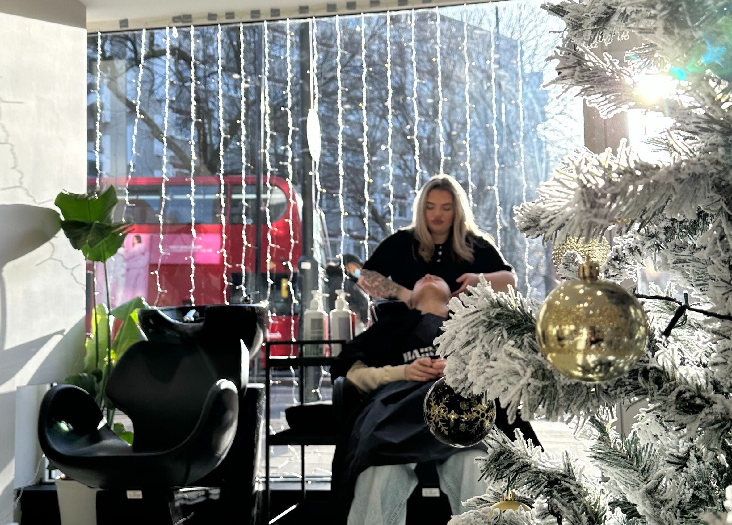 Festive salon scene at HairNova Angel in London, England, GB with stylist washing client's hair beside a decorated tree.