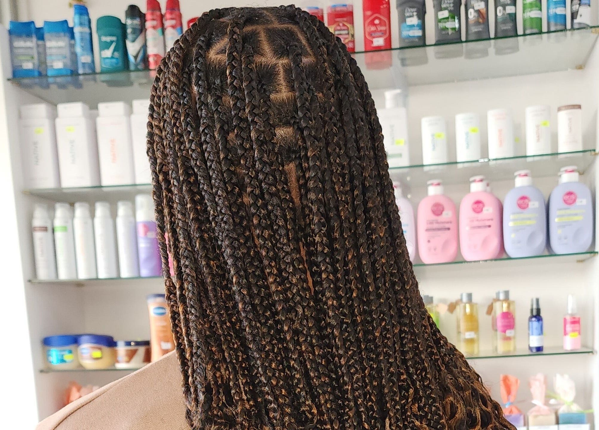 Intricate braids at Buti Haven By Yhen, Montego Bay, St. James Parish, JM. Shelves of beauty products in background.
