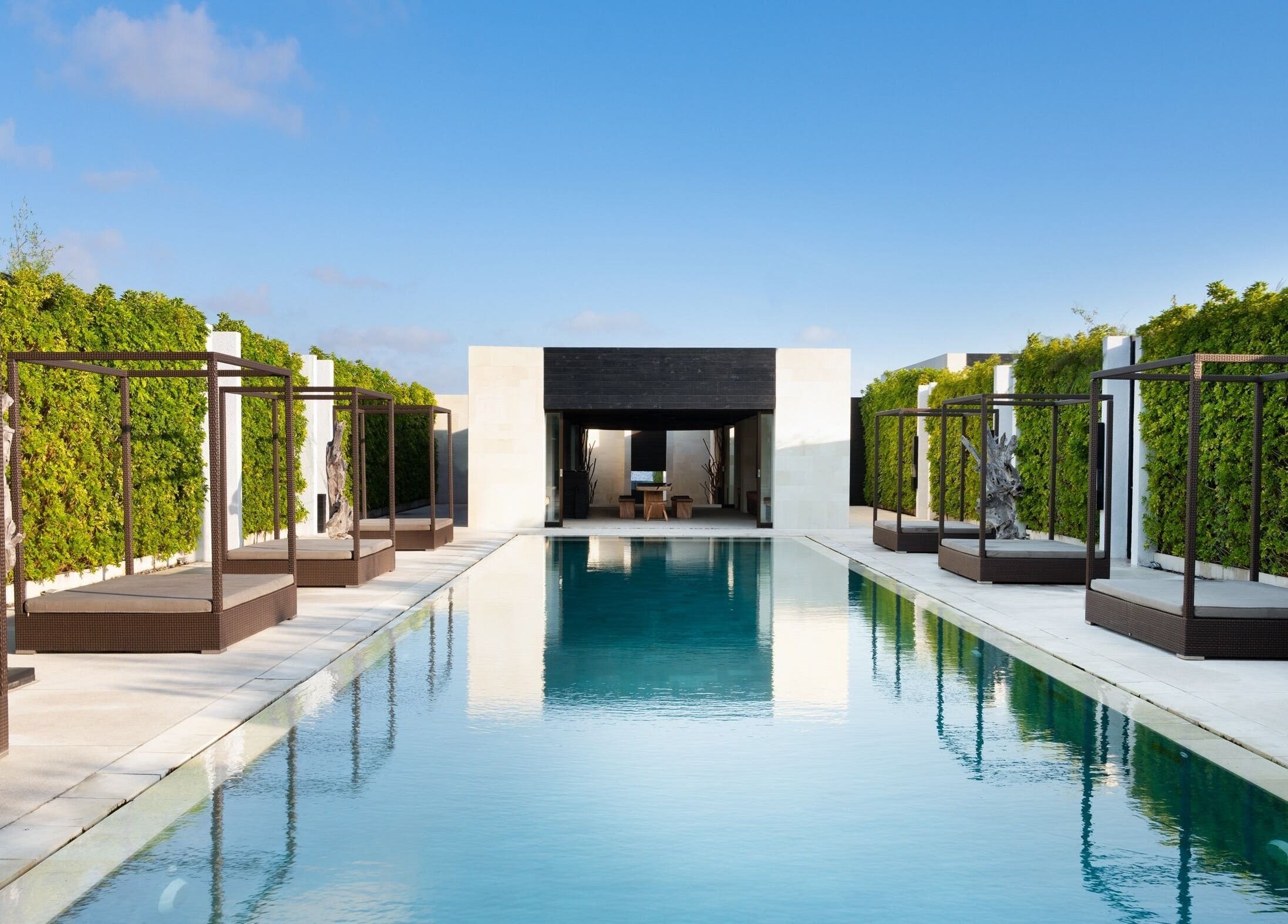 Luxury pool at eqUALIZE Spa, Kuta Utara, Bali, ID with serene cabanas and lush greenery under a blue sky.