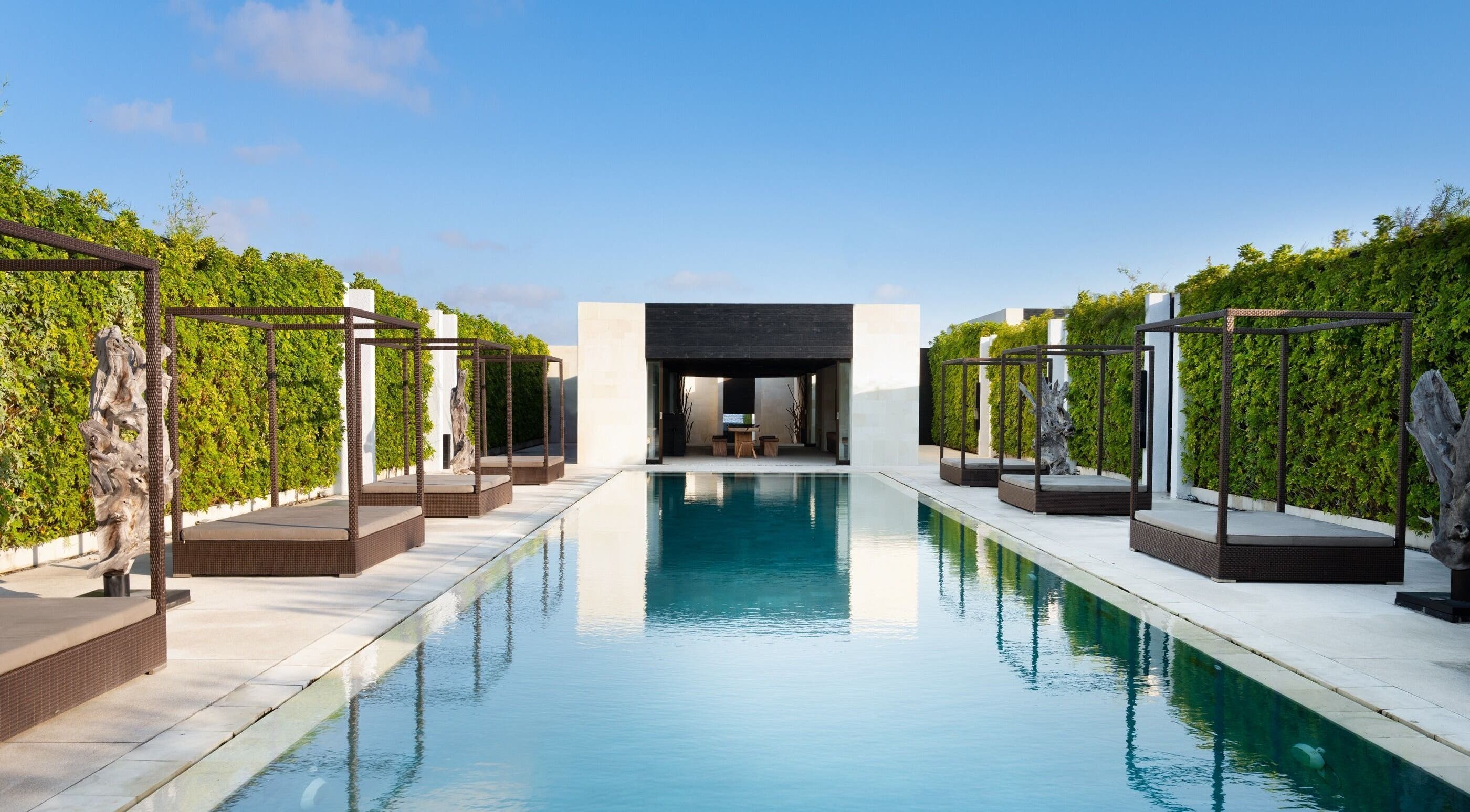 Luxury pool at eqUALIZE Spa, Kuta Utara, Bali, ID with serene cabanas and lush greenery under a blue sky.