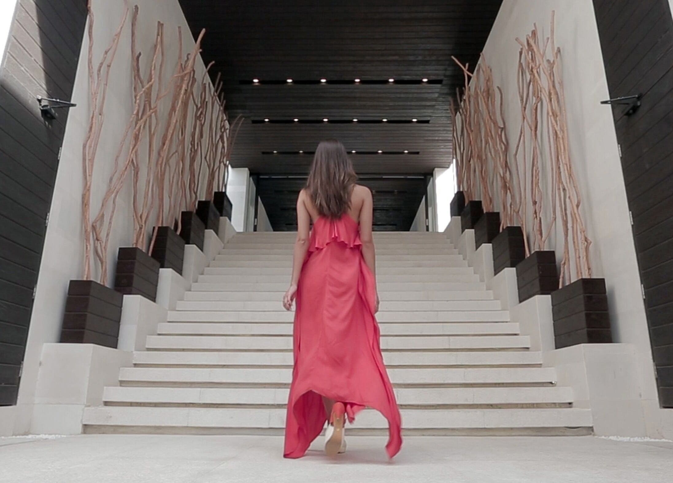 Woman in red dress ascending stairs at eqUALIZE Spa, Kuta Utara, Bali, ID showcasing modern interior design.