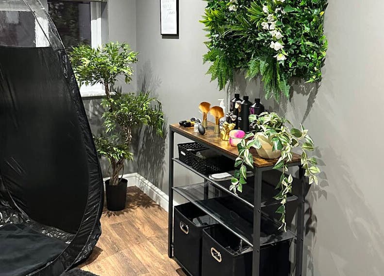 Relaxing corner at Sunless Glow, Leicester, England, GB featuring a tanning booth and lush greenery.