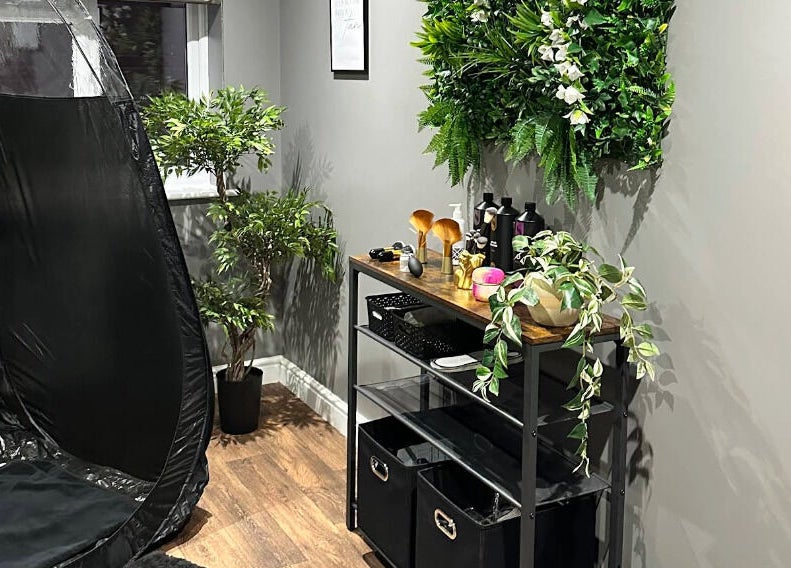 Relaxing corner at Sunless Glow, Leicester, England, GB featuring a tanning booth and lush greenery.