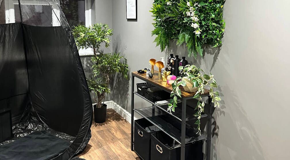 Relaxing corner at Sunless Glow, Leicester, England, GB featuring a tanning booth and lush greenery.
