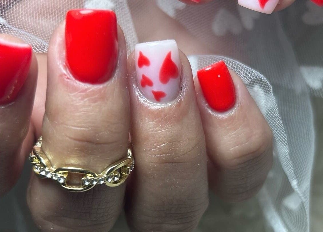 Diseño de uñas rojas con detalles de corazones en Mari Nails Ribadeo, Ribadeo, ES.