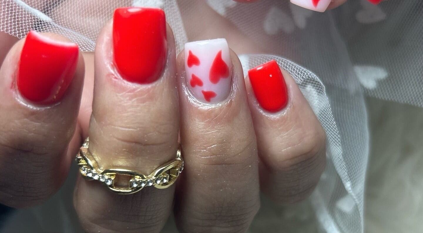 Diseño de uñas rojas con detalles de corazones en Mari Nails Ribadeo, Ribadeo, ES.