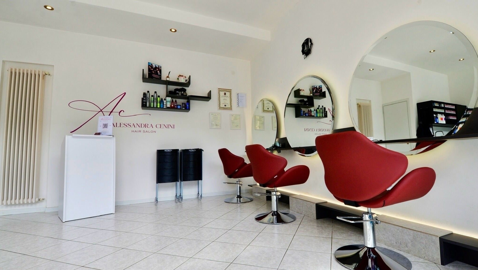 Interno del Alessandra Cenini Hair Salon a Ponte Di Legno, Lombardia: sedie rosse e specchi moderni.