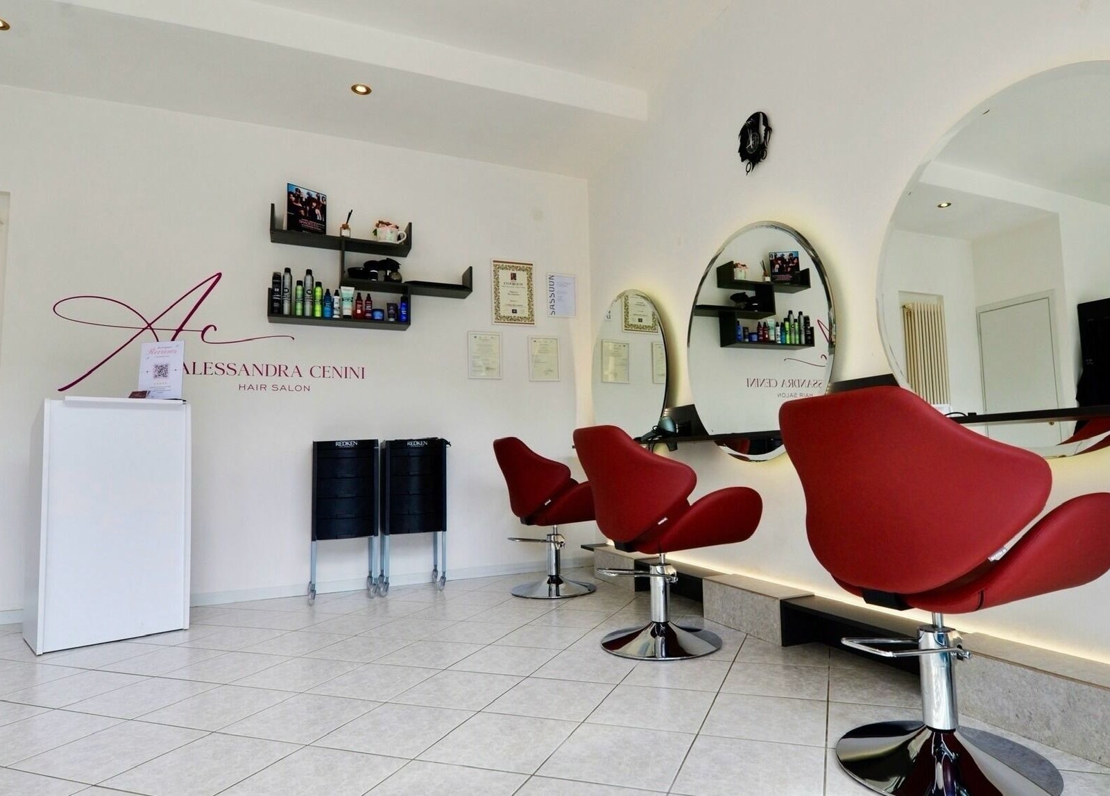 Interno del Alessandra Cenini Hair Salon a Ponte Di Legno, Lombardia: sedie rosse e specchi moderni.