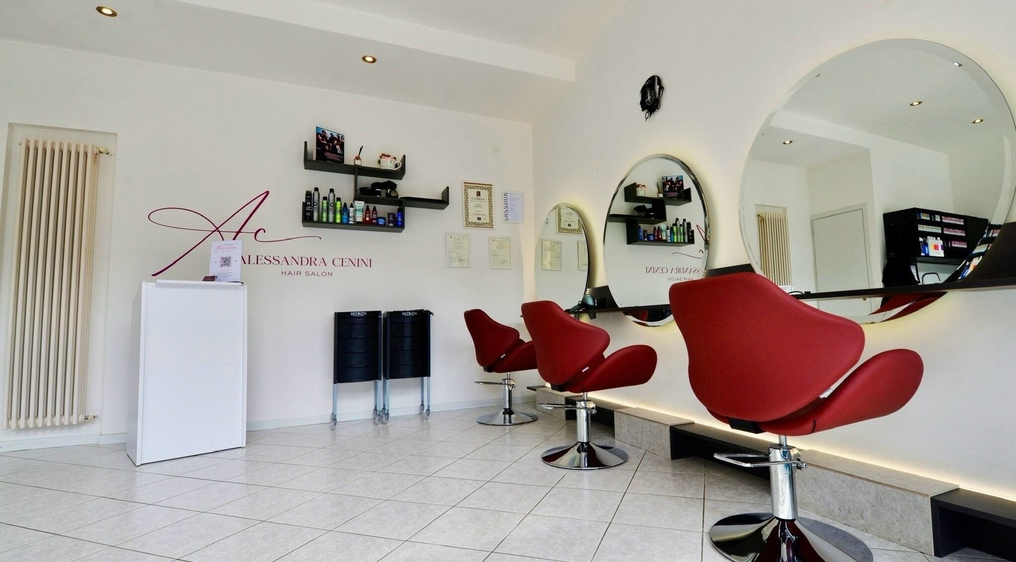 Interno del Alessandra Cenini Hair Salon a Ponte Di Legno, Lombardia: sedie rosse e specchi moderni.