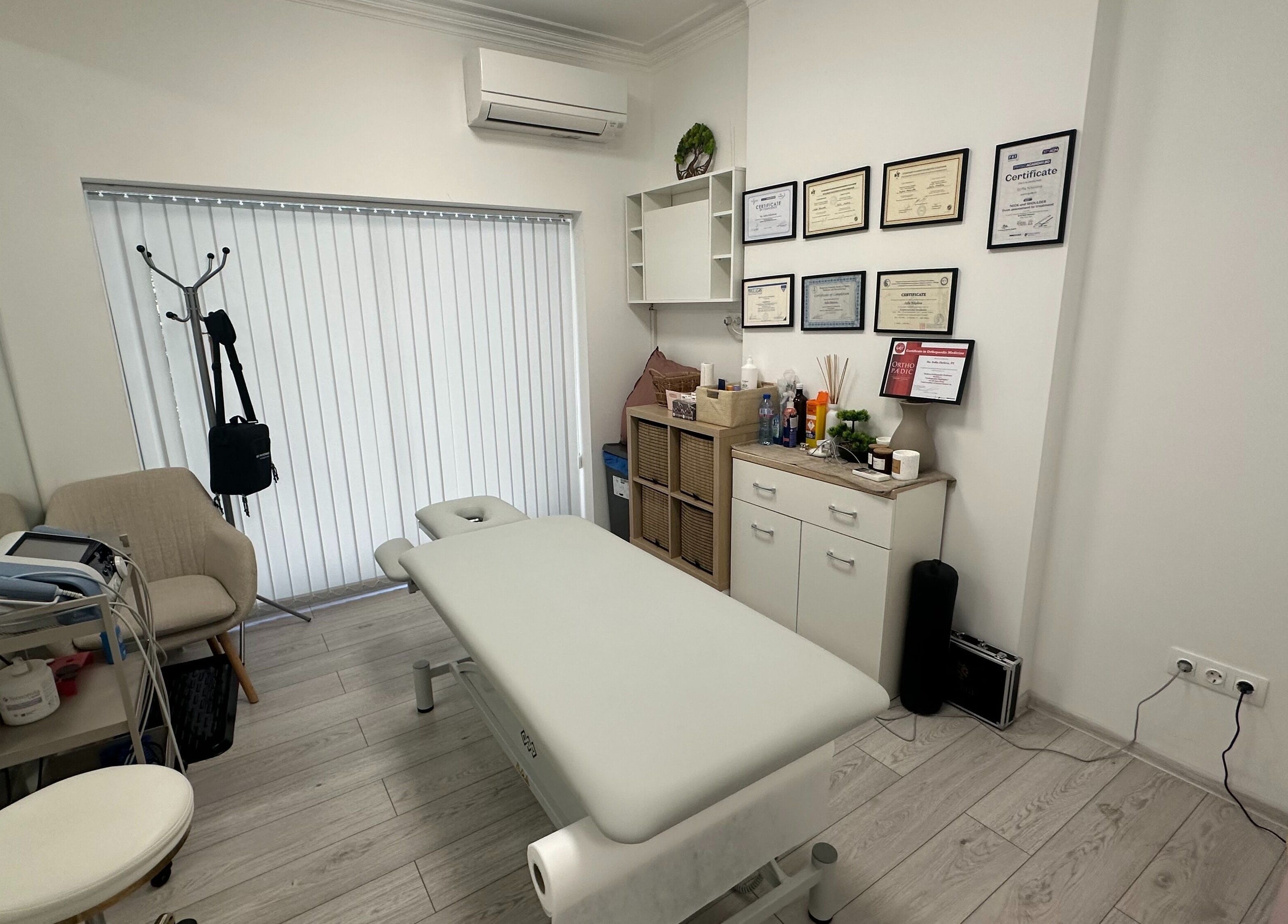 Интериор на SJ Physio & Pilates в София, Област София, BG, показващ масажна маса и сертификати.