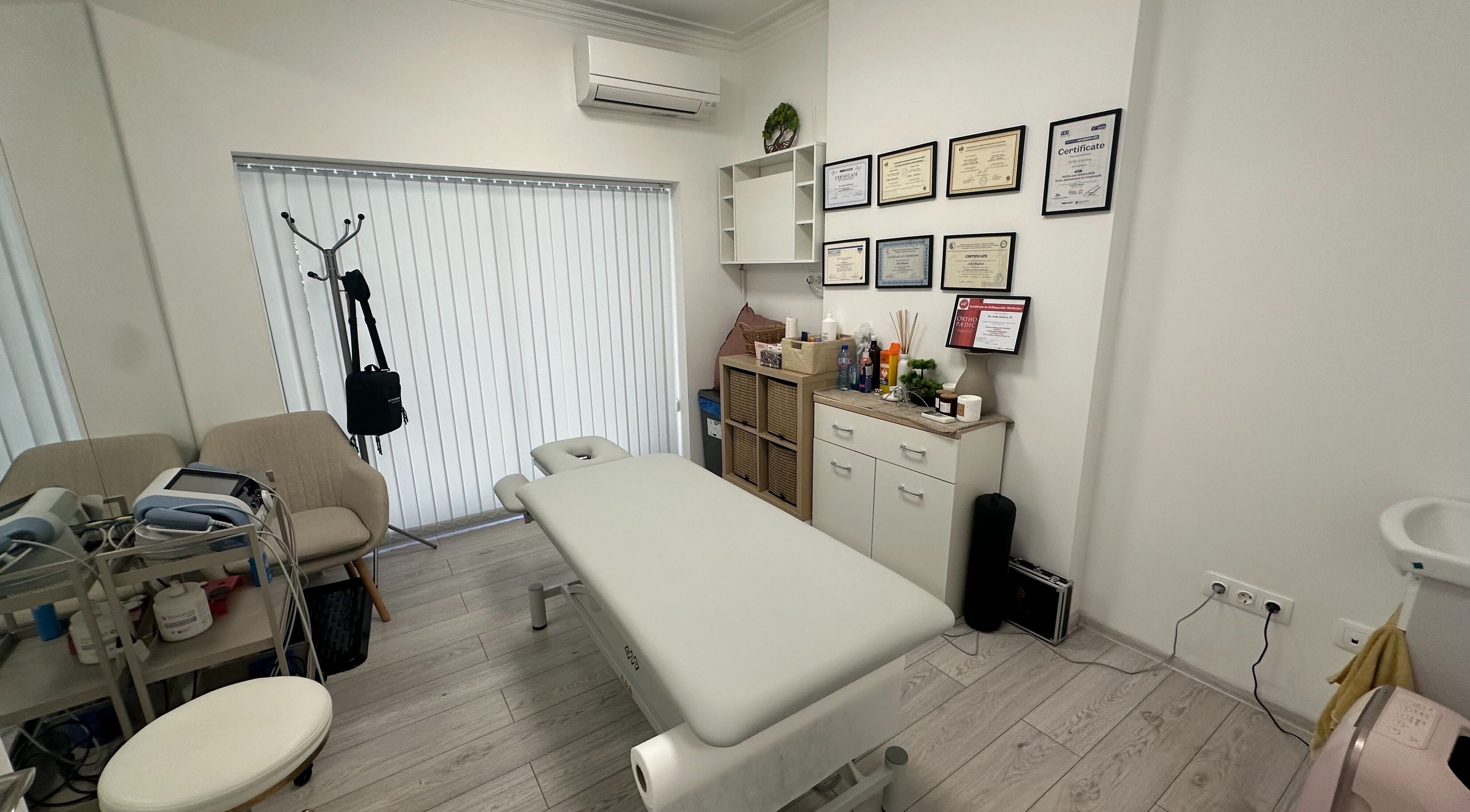 Интериор на SJ Physio & Pilates в София, Област София, BG, показващ масажна маса и сертификати.