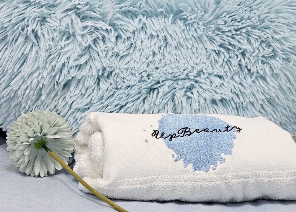 Toalha personalizada Upbeautysalon em Albufeira, Faro, PT, sobre almofada azul macia e flor decorativa.