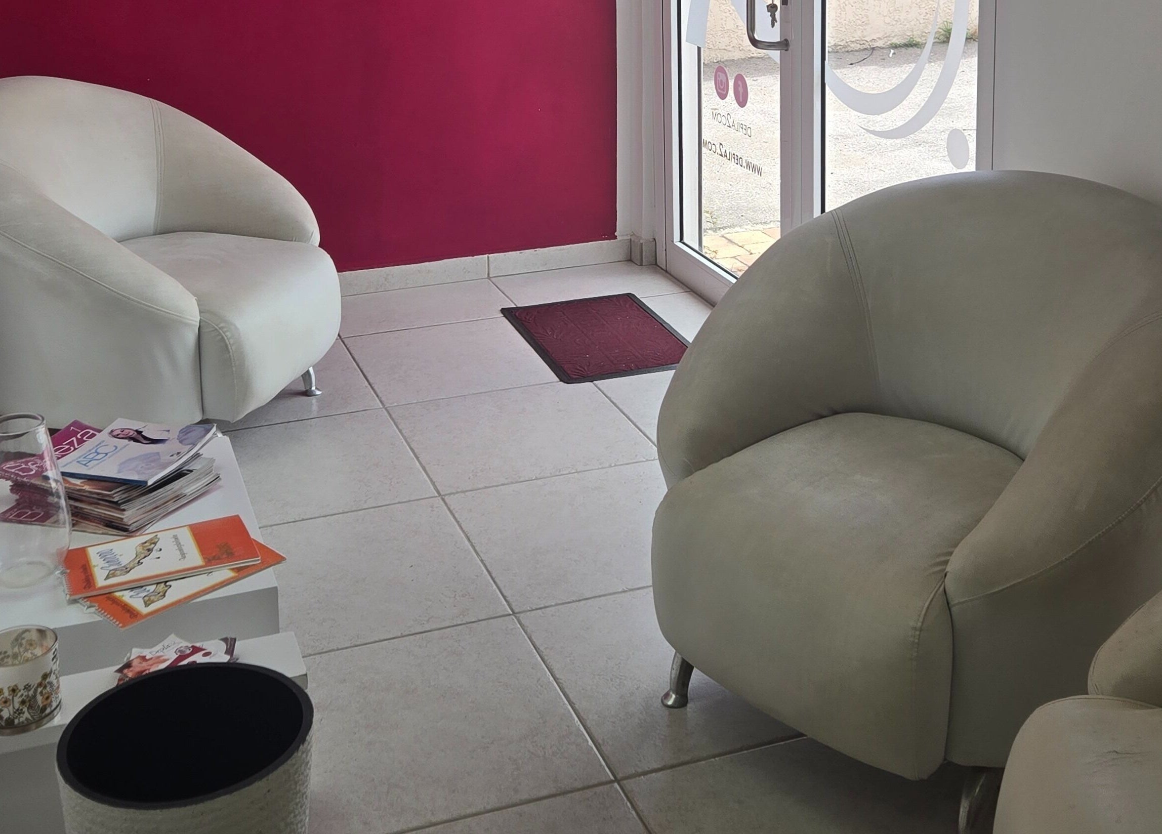 Sala de espera acogedora en Depila2, Willemstad, CW con sillas blancas y revistas.