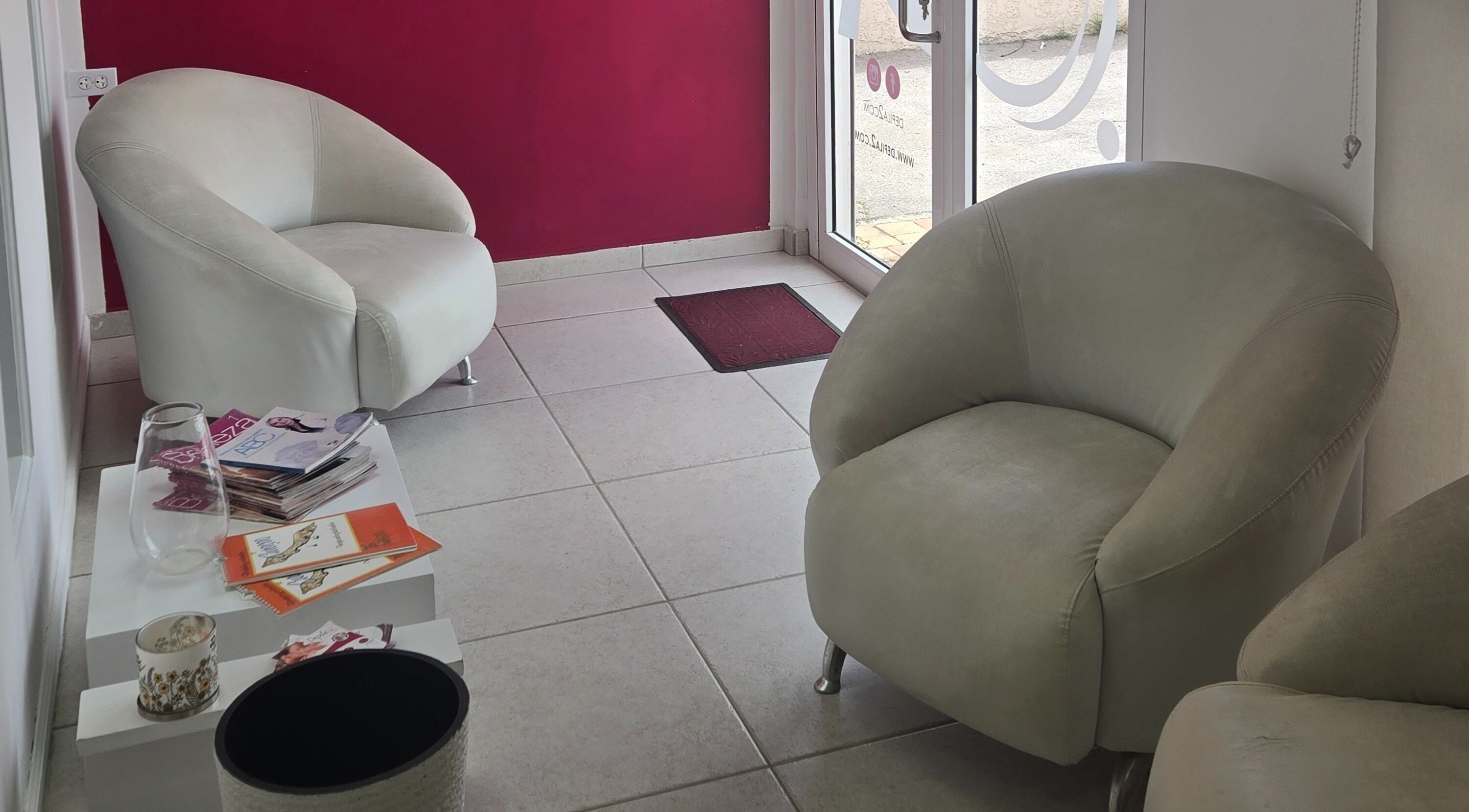 Sala de espera acogedora en Depila2, Willemstad, CW con sillas blancas y revistas.