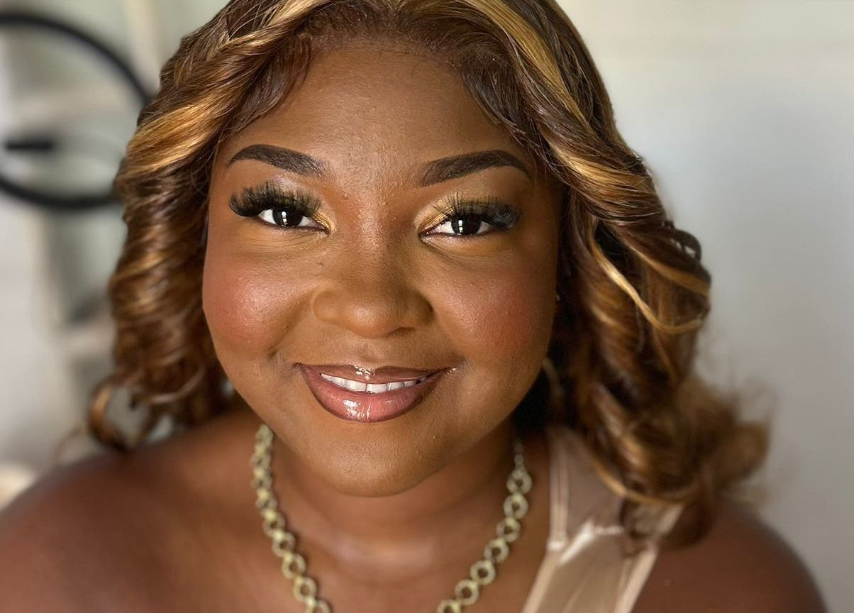 A smiling woman at Jibeautyplus in Roseau, Saint George Parish, DM, showcasing elegant makeup and curls.