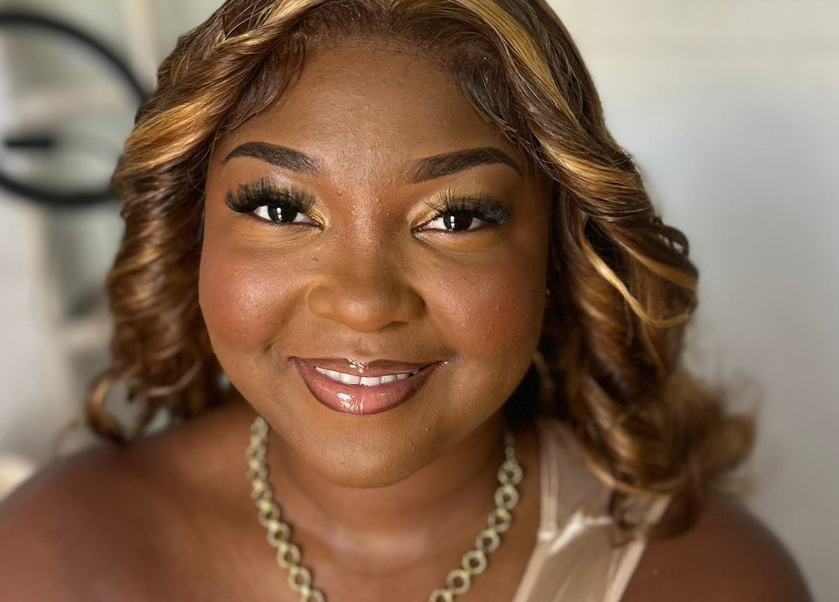 A smiling woman at Jibeautyplus in Roseau, Saint George Parish, DM, showcasing elegant makeup and curls.