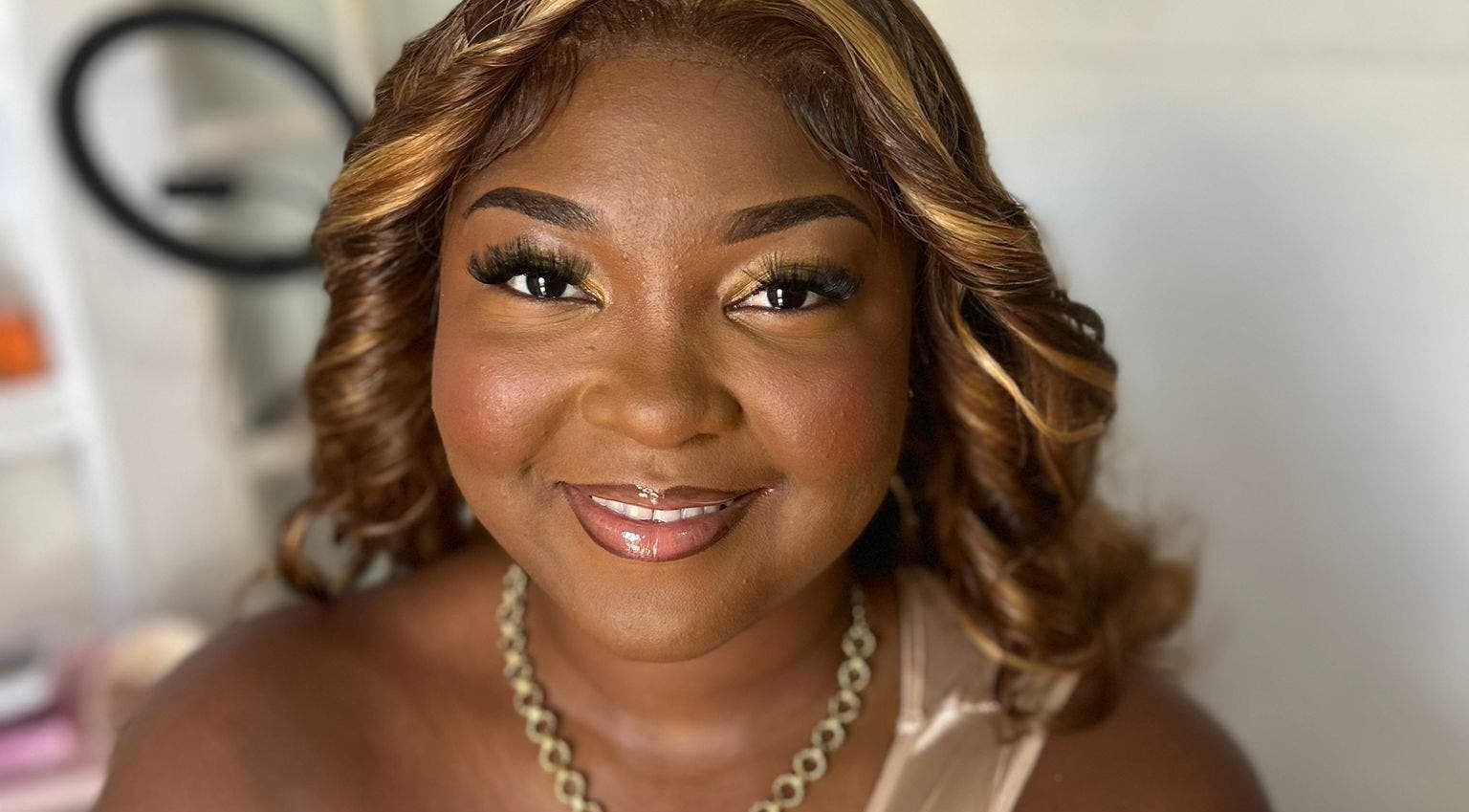 A smiling woman at Jibeautyplus in Roseau, Saint George Parish, DM, showcasing elegant makeup and curls.