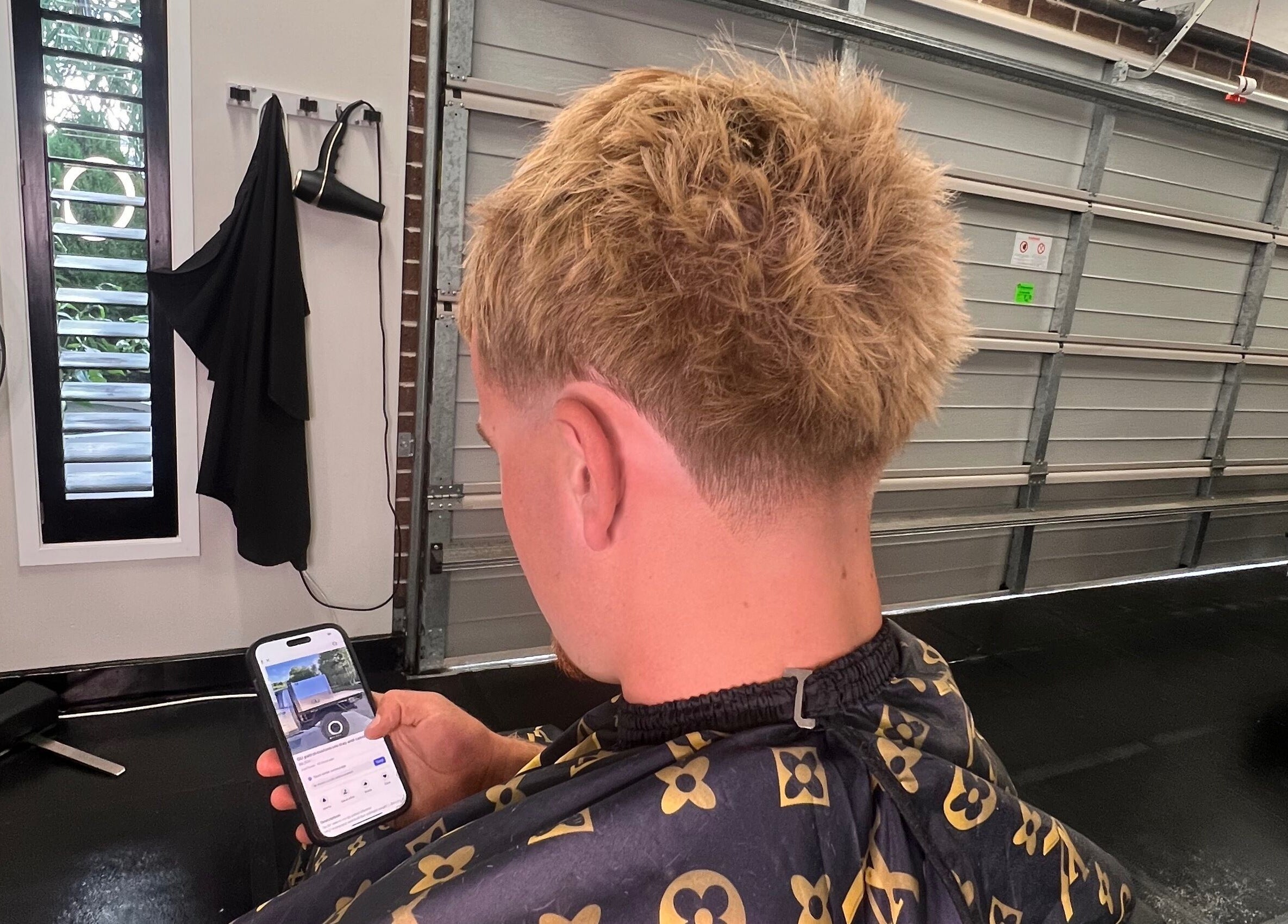 Client with stylish haircut at Chuckz Cutz, Melbourne, Victoria, AU, checking phone in barber chair.