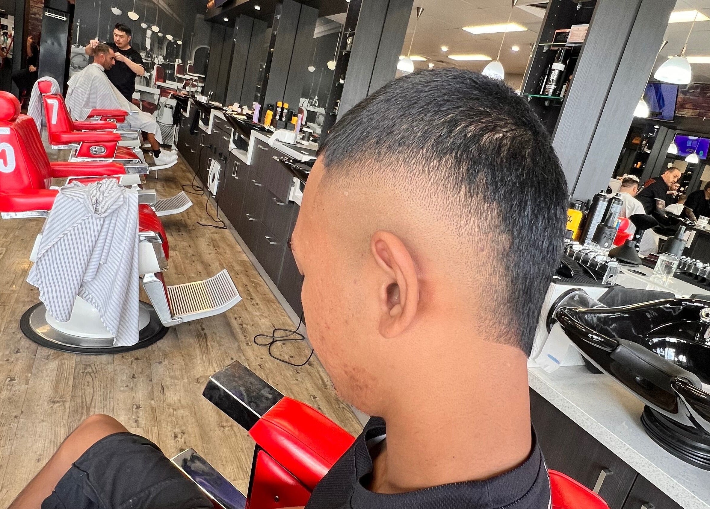 Client getting a haircut at Chuckz Cutz, modern interior with red chairs, Melbourne, Victoria, AU.