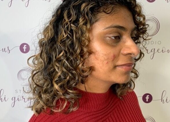 Woman with curly hair in front of Studio Hi Gorgeous banner in Alfredton, Victoria, AU.