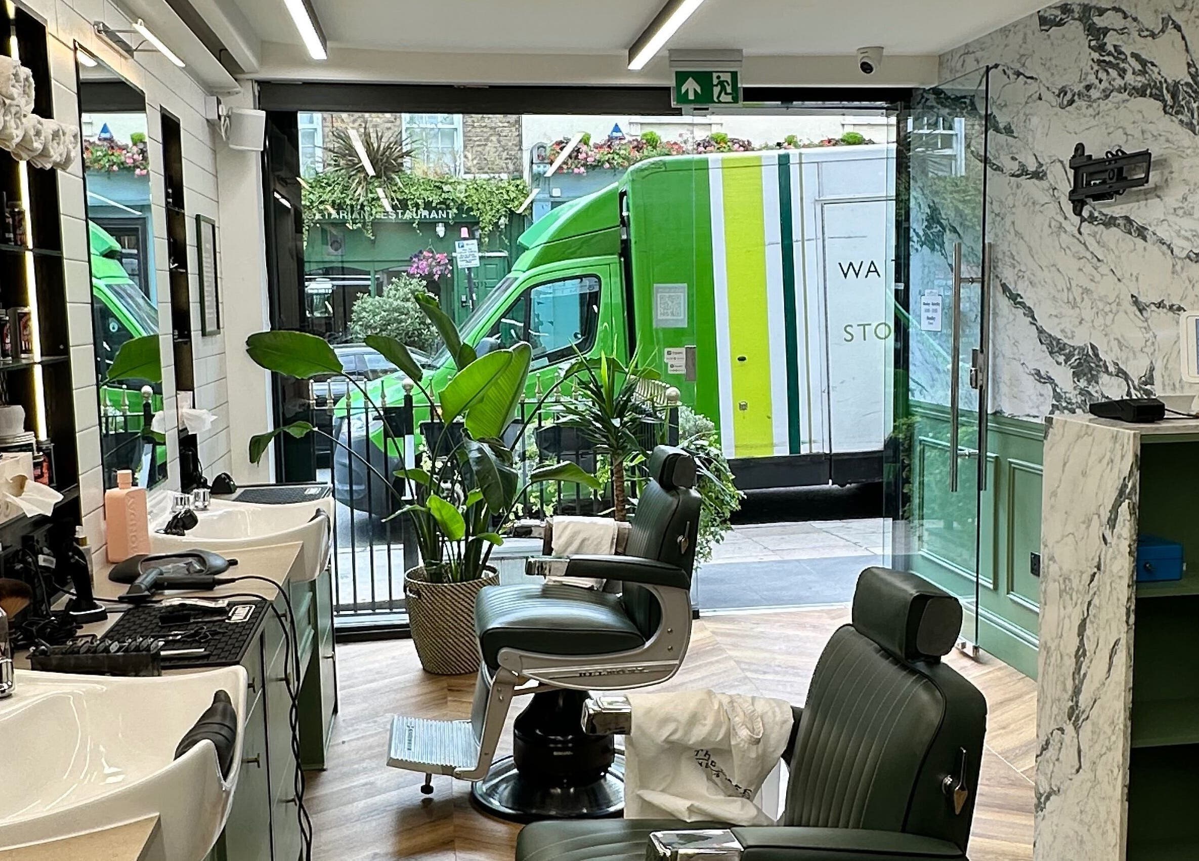 Stylish barber setup at The Axe Club - Euston in London, England, GB, featuring green chairs and marble decor.