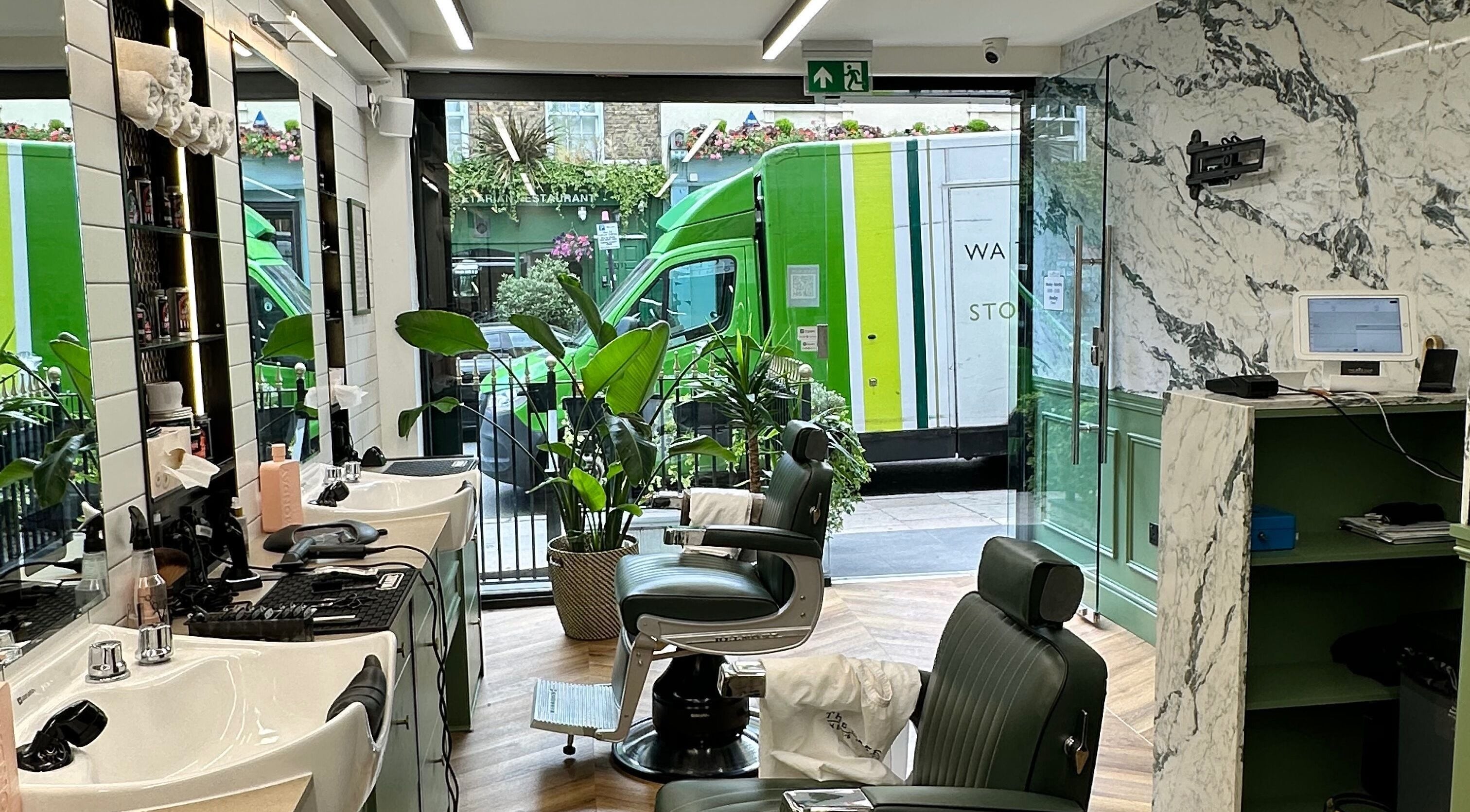 Stylish barber setup at The Axe Club - Euston in London, England, GB, featuring green chairs and marble decor.