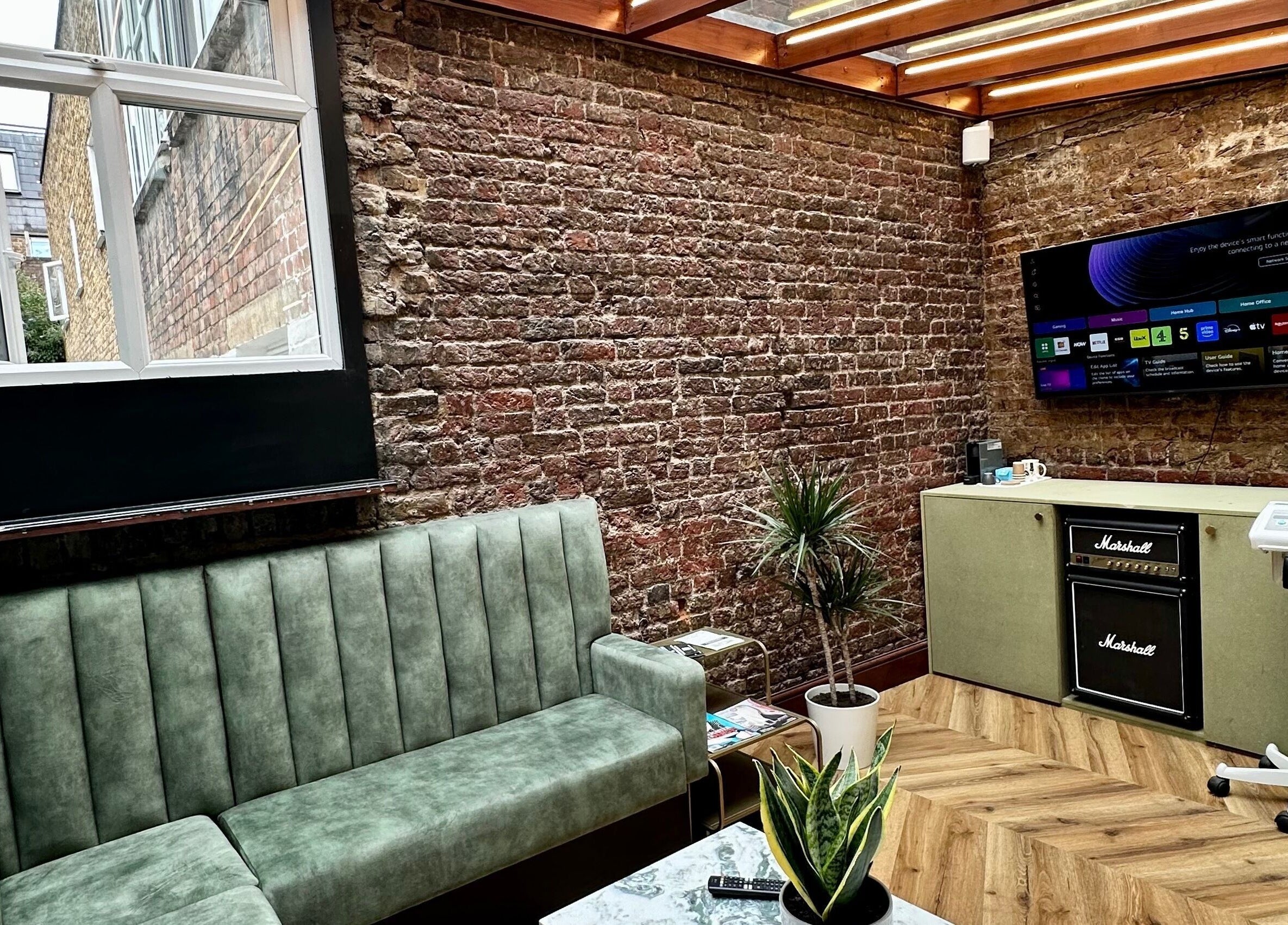 Stylish brick-walled lounge at The Axe Club - Euston, London, England, GB with green sofas and indoor plants.