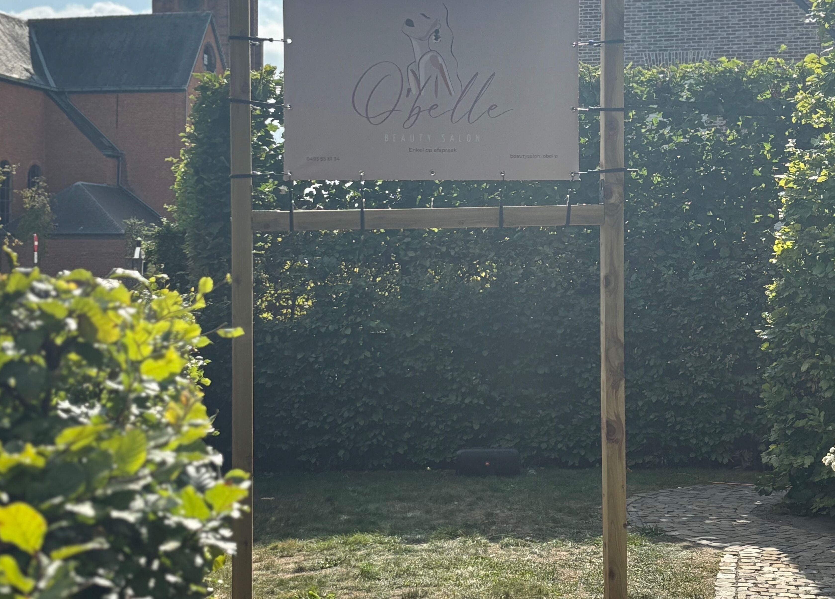 Ingangsbord van O'belle in Heist-op-den-berg, Vlaams Gewest, BE, omgeven door groene heggen.