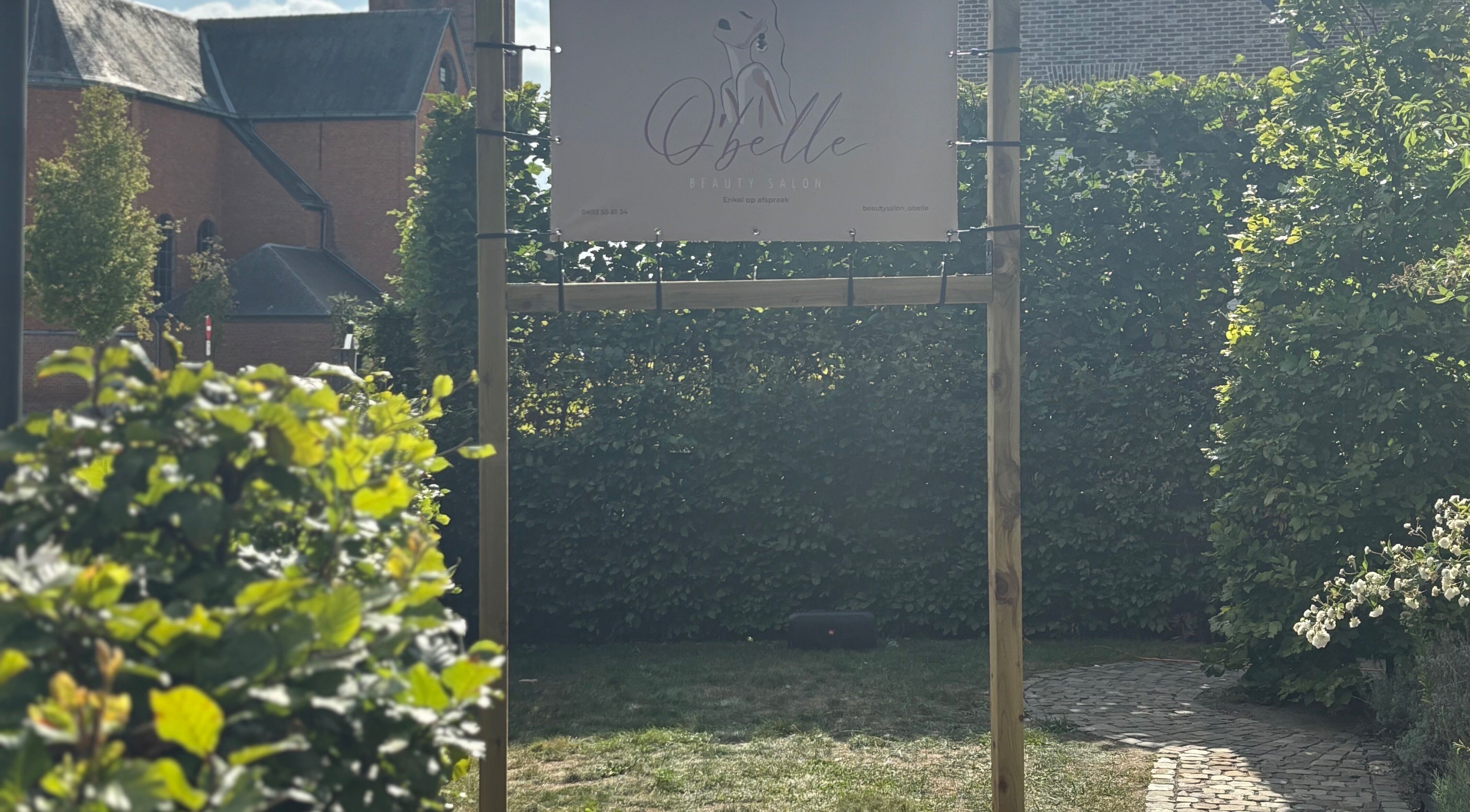 Ingangsbord van O'belle in Heist-op-den-berg, Vlaams Gewest, BE, omgeven door groene heggen.