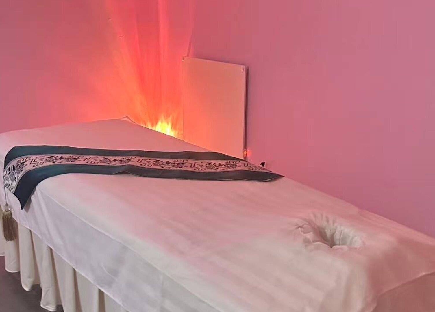 Calming massage therapy room at Yo Spa, London, England, GB, featuring a cozy bed and ambient pink lighting.