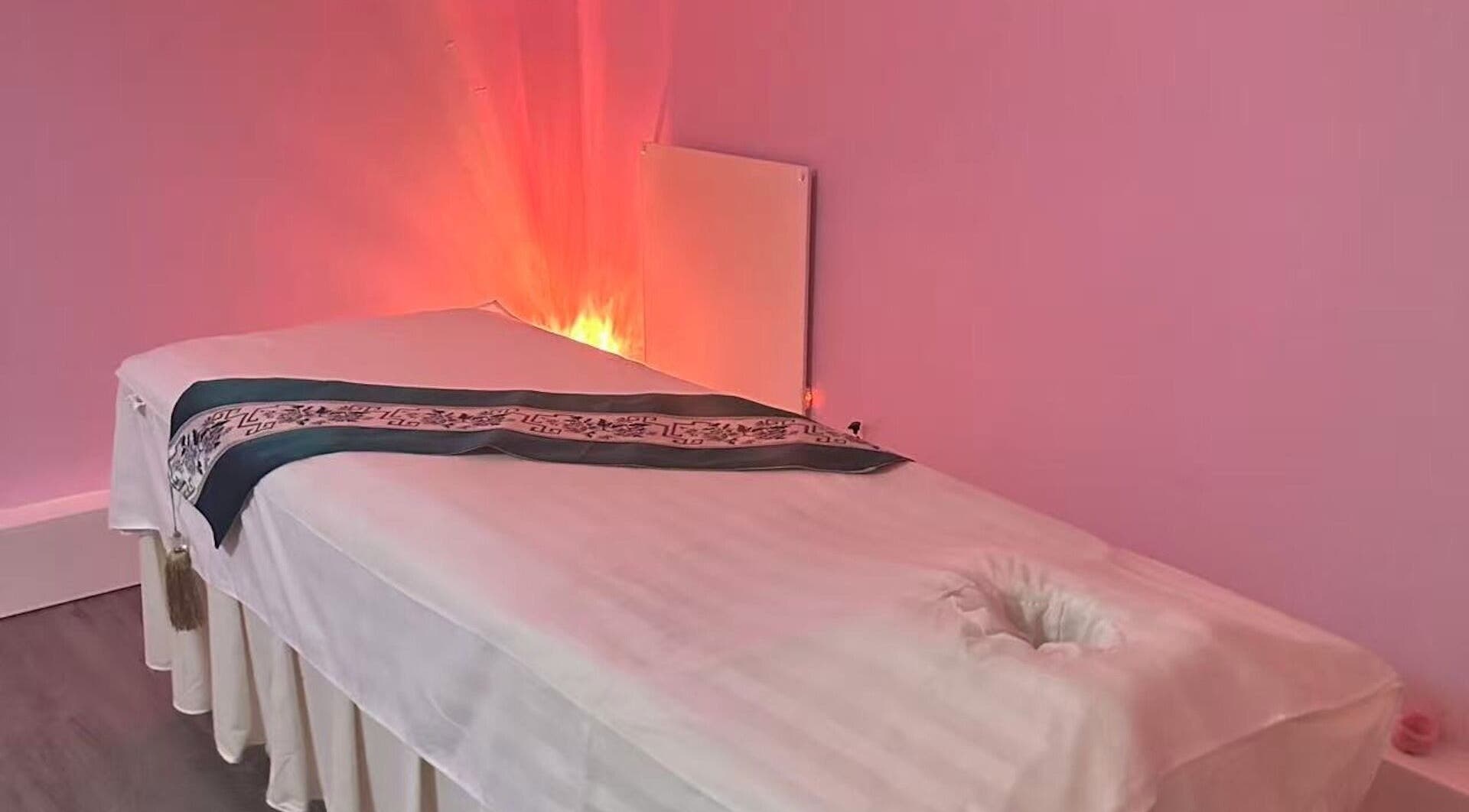 Calming massage therapy room at Yo Spa, London, England, GB, featuring a cozy bed and ambient pink lighting.