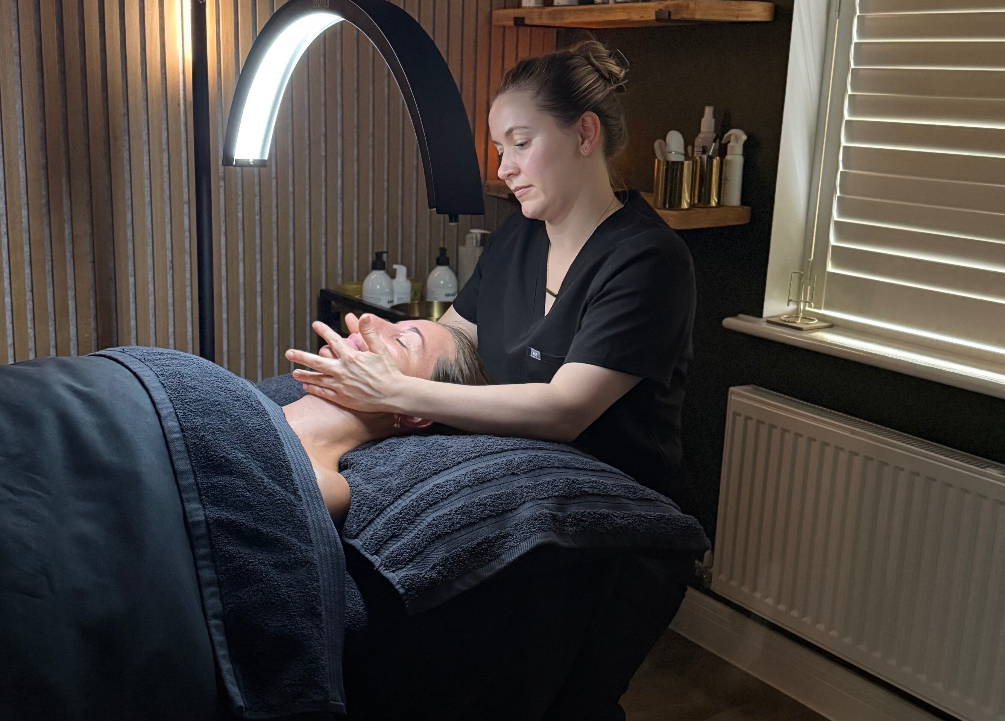 Skincare treatment at Glow and Renew Skincare, Ash, England, GB. Therapist massages client's face under cozy lighting.