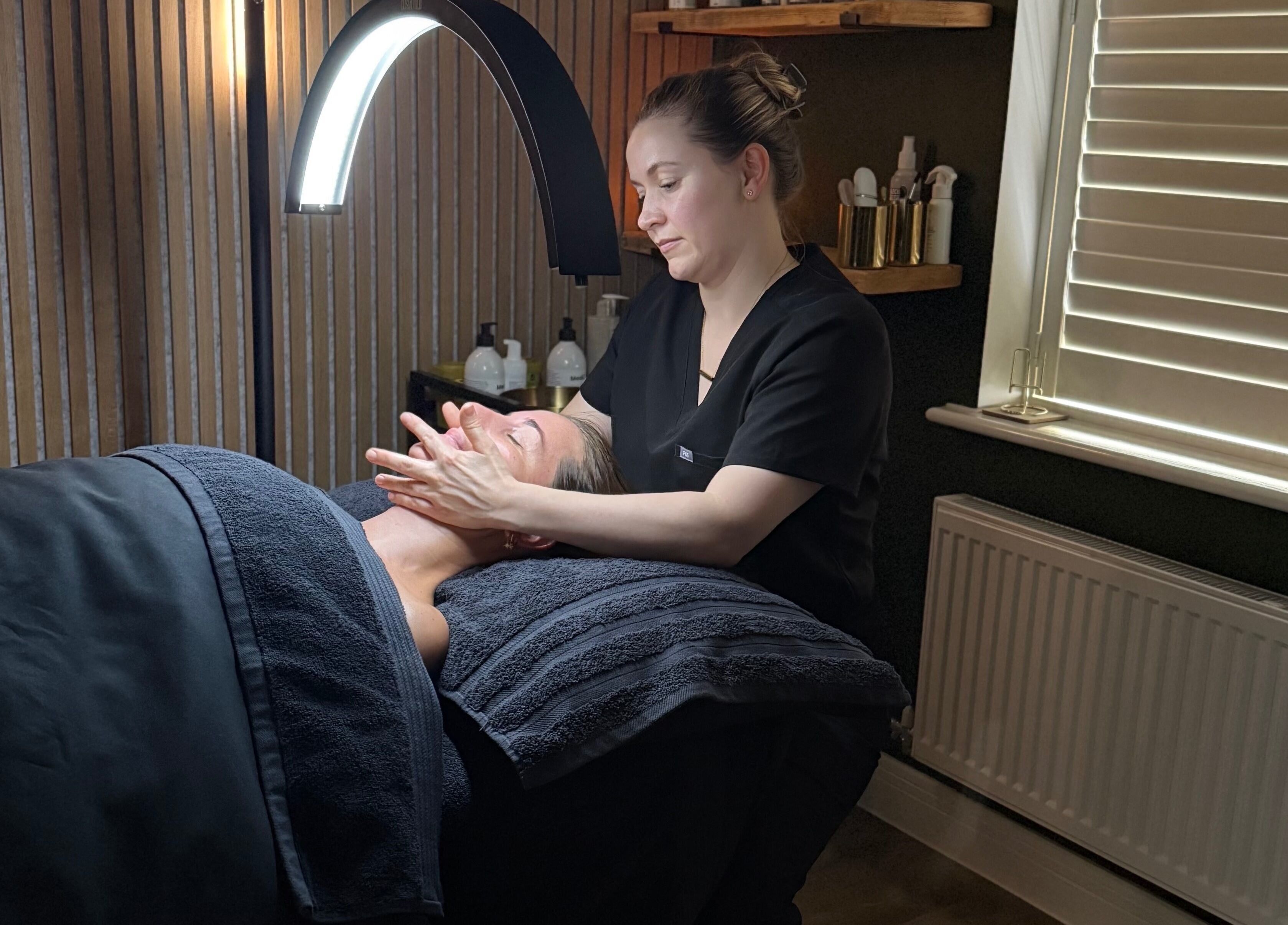 Skincare treatment at Glow and Renew Skincare, Ash, England, GB. Therapist massages client's face under cozy lighting.
