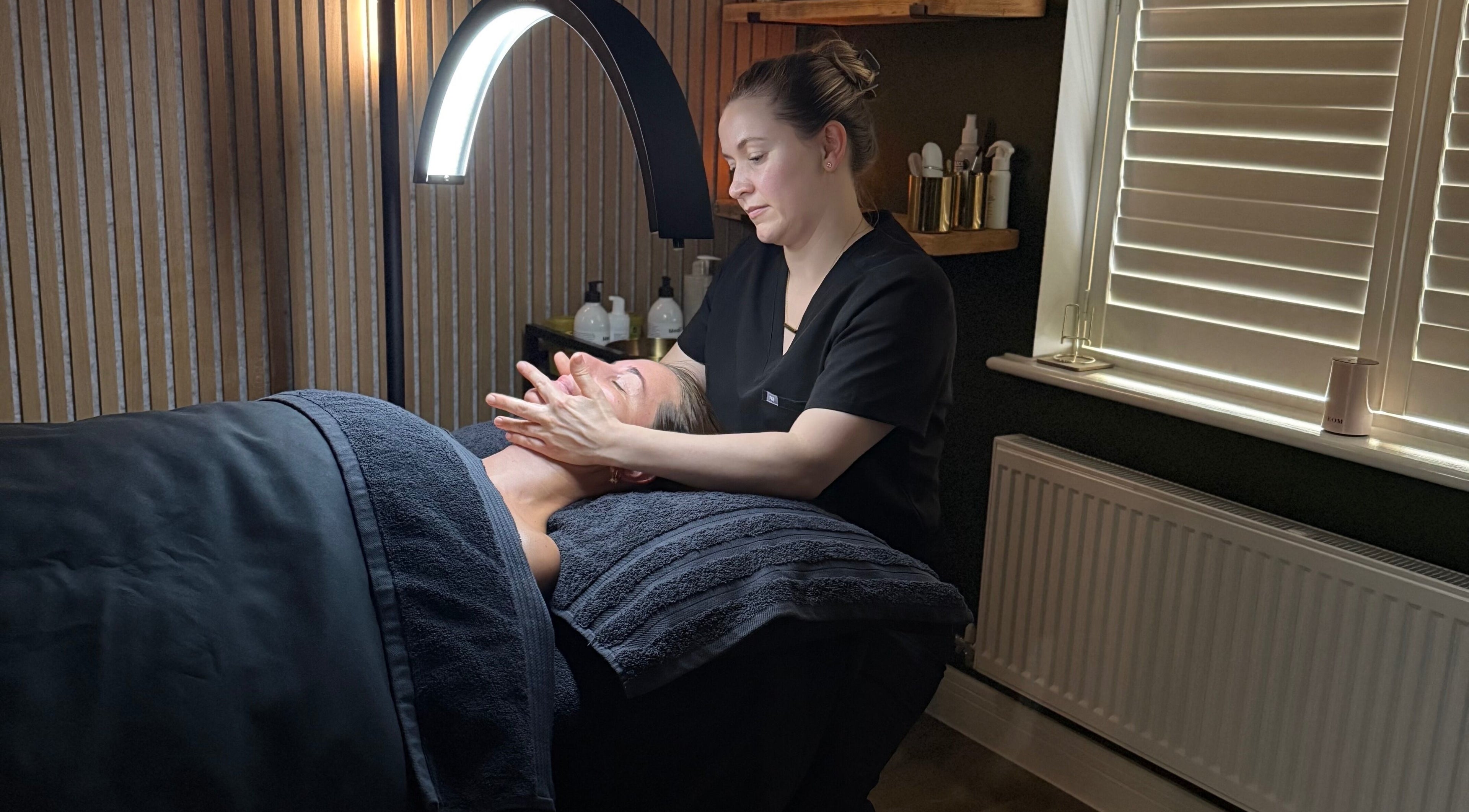 Skincare treatment at Glow and Renew Skincare, Ash, England, GB. Therapist massages client's face under cozy lighting.
