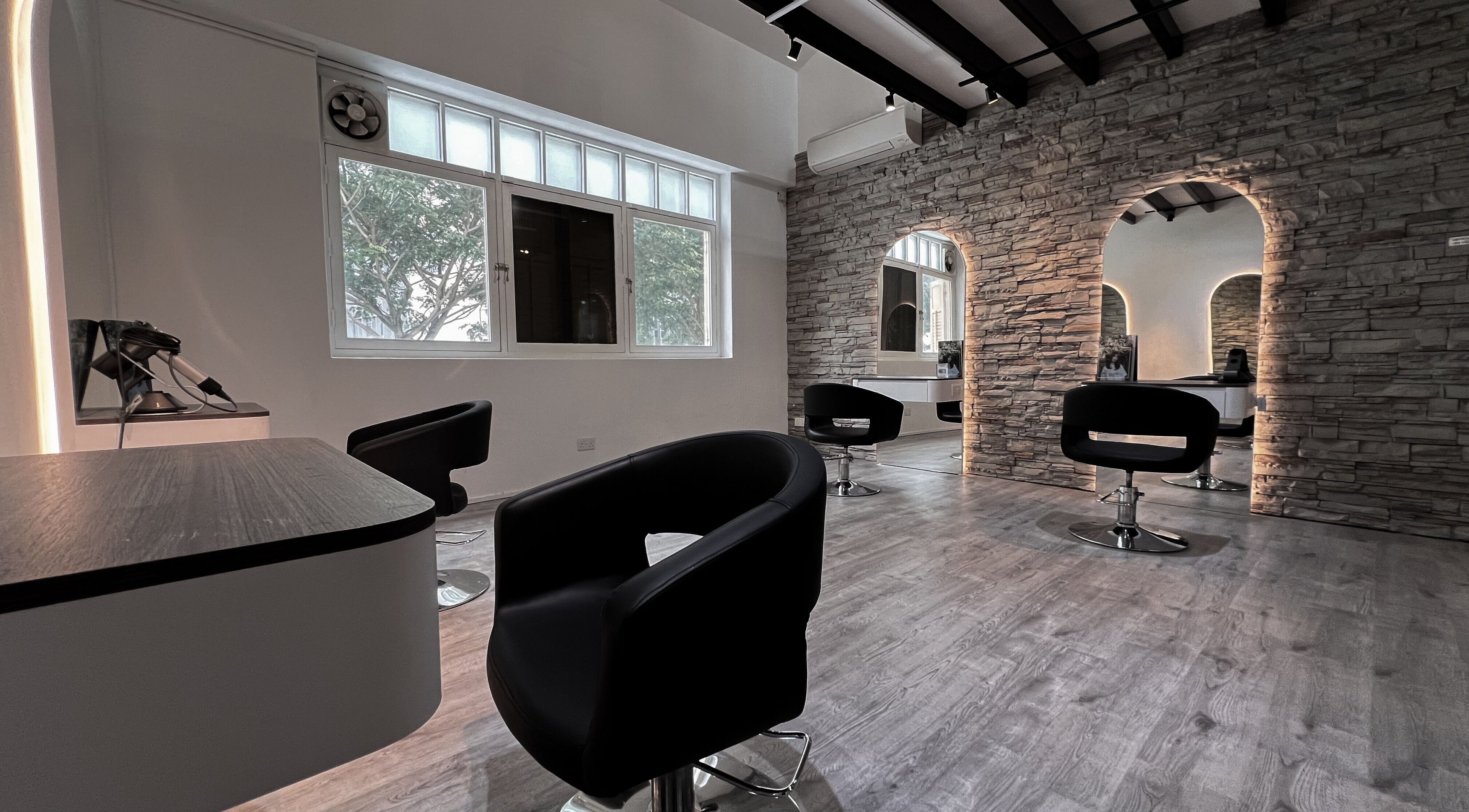 Modern interior of OHANA by MUSUBI BOUTIQUE HAIR SALON, Singapore, Singapore, SG, with sleek chairs and stone walls.