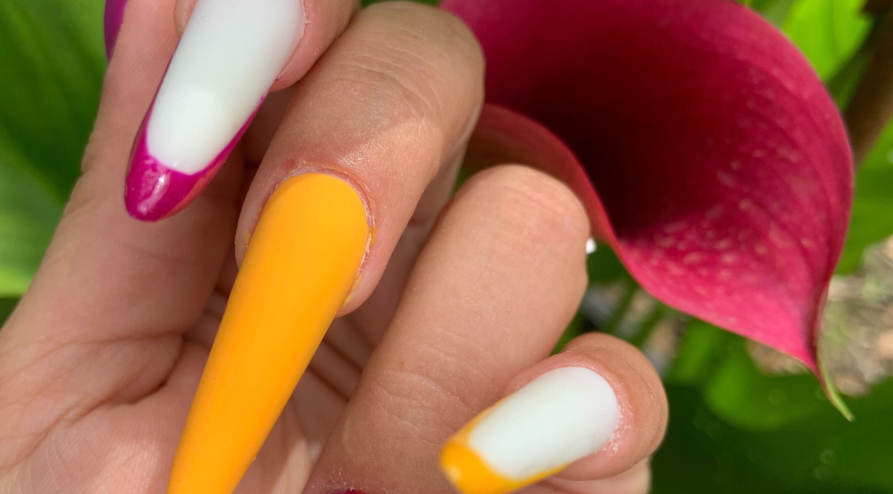 Ongles multicolores élégants chez L’Amazones Nails, Gabian, Occitanie, FR, avec fleurs arrière-plan.